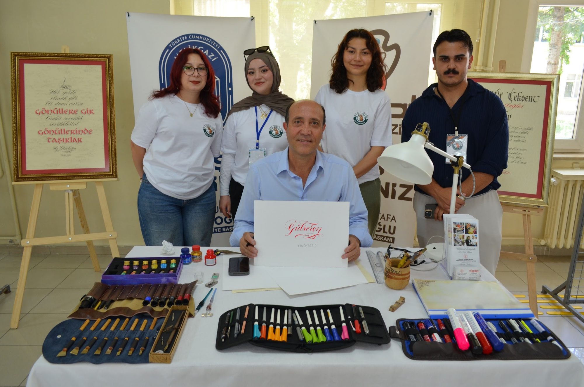 Mustafa Türkmen, Sanat Melikgazi'deki kurs masasında öğrencileriyle; önünde renkli kaligrafi kalemleri